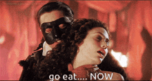 a man in a mask holds a woman 's neck and says " go eat ... now "