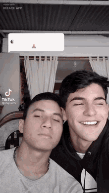 two young men are posing for a picture and one of them has a tik tok app on his phone