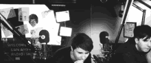 a black and white photo of two men sitting in front of microphones in a radio studio .