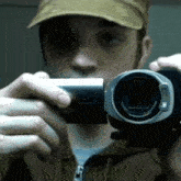 a man wearing a hat is taking a picture with a camera that says olympus on it