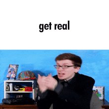 a man with glasses is clapping in front of a blue wall with the words get real written on it