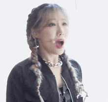 a woman with braids is wearing a black jacket and a microphone in her mouth .