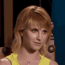 a woman wearing a yellow tank top and a necklace is looking at the camera .