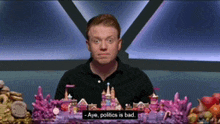 a man sitting at a table with a sign that says " aye politics is bad "