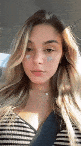 the woman is wearing a striped shirt and a necklace and has stars on her face .