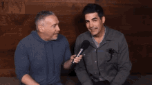 two men are sitting next to each other and one is holding a microphone in his hand