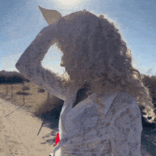 a woman wearing a white lace top stands on a dirt road