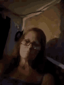 a woman wearing glasses is sitting in a dark room in front of a wall .
