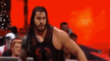 roman reigns is a wrestler in a black tank top standing in a ring .