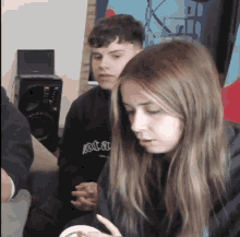 a girl wearing a black sweatshirt that says ' jota ' on it sits next to a boy