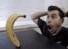 a man is sitting at a table with his mouth open and a banana in the background .