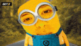 a yellow minion wearing overalls and goggles with a getx logo behind him