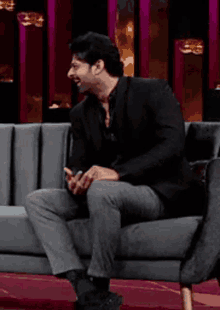 a man in a black suit is sitting on a couch laughing