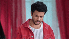 a man in a red jacket and white sweater is looking down .