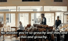 a man in a suit is talking to a woman in a restaurant while a woman sits at a table in the background .