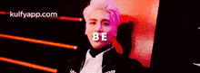 a man in a suit is standing in front of a red wall with the words `` be '' written on it .