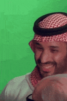 a man wearing a head scarf and a turban is smiling in front of a green screen .