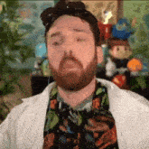 a man with a beard and glasses is wearing a white coat and a colorful shirt .