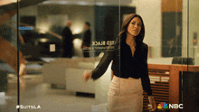 a woman standing in front of a glass door with nbc on the bottom right