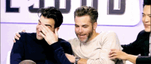 two men are sitting next to each other laughing and one of them is covering his face .