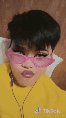 a girl wearing a yellow shirt and pink sunglasses has a tiktok watermark on her face