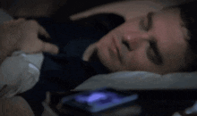 a man in a blue shirt is sleeping in a dark room with his eyes closed
