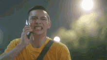 a man in a yellow shirt is talking on a cell phone and making a funny face .