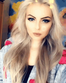 a woman with long blonde hair and blue eyes is wearing a sweater with hearts on it