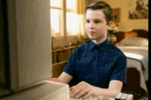 a boy in a blue shirt is typing on a computer keyboard .