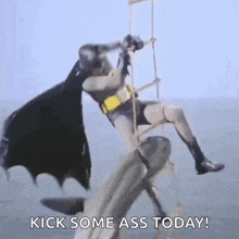 a man in a batman costume is hanging from a rope while a shark attacks him .