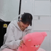 a woman is holding a pink teddy bear in her lap and smiling .