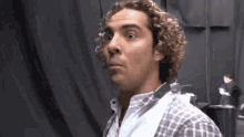 a man with curly hair is making a funny face in front of a black curtain