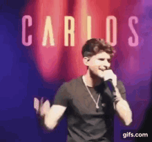 a man is singing into a microphone on a stage in front of a red curtain .