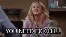 a woman is sitting at a table with her hands up and the words `` you need to chill '' .