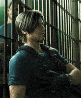 a man in a blue shirt is standing in front of a jail cell .