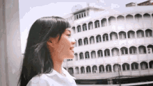 a woman in a white shirt is standing in front of a building with arched windows .