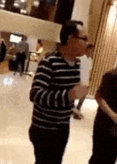 a man in a striped sweater and glasses is standing in a room .