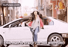 a woman is standing next to a white car and saying `` this man is crazy , i 'm not with him ! ''