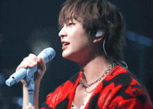 a man in a red and black sweater sings into a blue microphone
