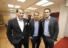 three men in suits are posing for a picture together in a room .