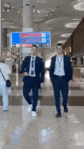 two men in suits and ties are walking down a hallway at an airport .