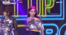 a girl with pink hair is dancing on stage in front of a neon sign that says mbc m