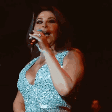 a woman is singing into a microphone in a blue dress