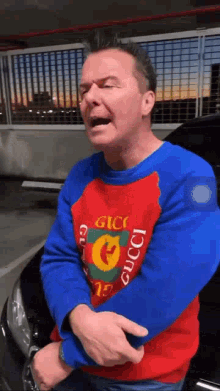 a man wearing a gucci sweater is standing in front of a car