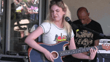 a woman playing a guitar in front of a man wearing a shirt that says the morning