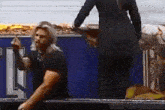 a man is kneeling down in front of a blue wall while a woman is standing behind him .