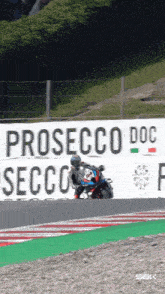 a man riding a motorcycle on a race track with a sign that says prosecco doc