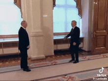 two men in suits shake hands in a hallway with a tiktok watermark