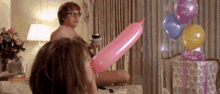 a man is holding a pink balloon while a woman blows up a pink balloon in a living room .