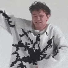a man is wearing a white sweater with black spots on it and dancing .
